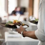 photo resserrée sur l'épaule et le bras d'un serveur tenant une assiette à apporter au client